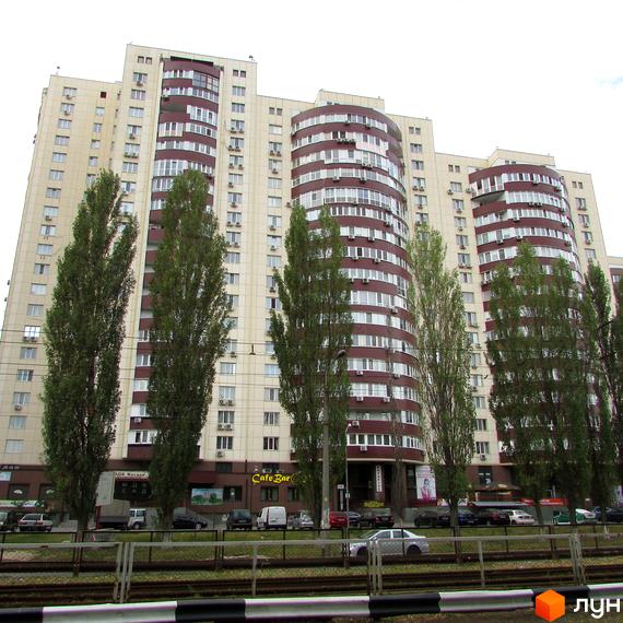 Житловий комплекс Парковий: багатоповерховий будинок зі світлим фасадом та округлими секціями. Перед ним високі дерева та дорога з автомобілями.