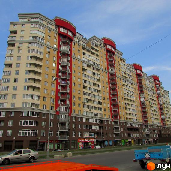 Житловий комплекс Ліко-Град 3: багатоповерховий будинок з бежевими, червоними та коричневими фасадами, балконами. На перших поверхах магазини, поруч дорога.