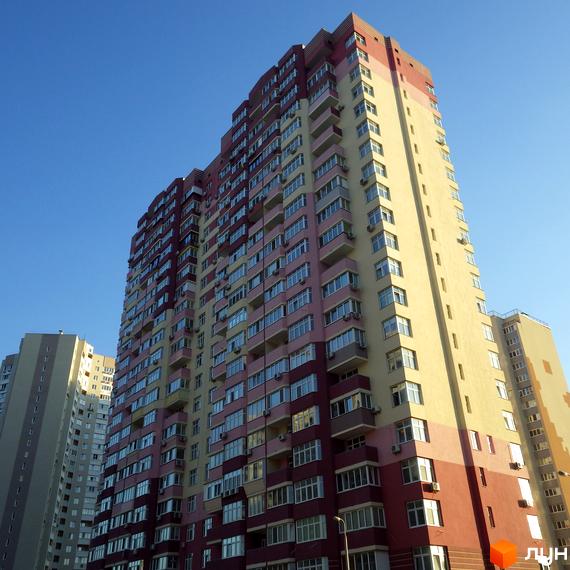 Вигляд житлового комплексу Молодіжний квартал з фасадом, оздобленим вікнами та балконами. Прибудинкова територія з зеленими насадженнями.