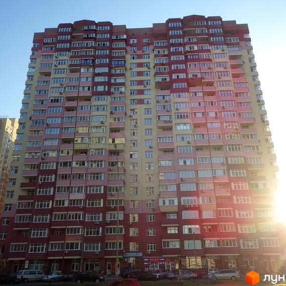 Житловий комплекс Молодіжний квартал з яскравим фасадом та великою кількістю вікон. Прибудинкова територія з автомобілями та магазинами на першому поверсі.