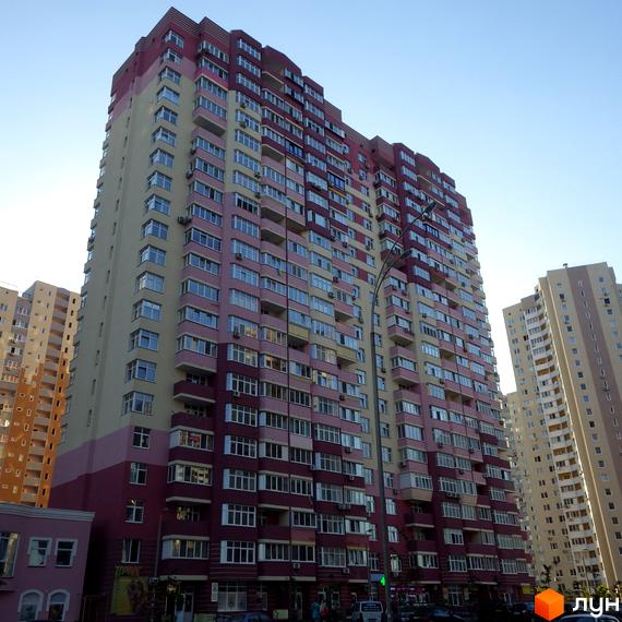 Житловий комплекс Молодіжний квартал з сучасним фасадом та великою кількістю вікон. Прибудинкова територія містить зелені насадження та парковку.