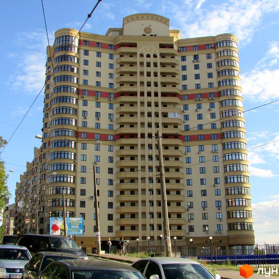 Златоустівський житловий комплекс: висотна будівля з вигнутим фасадом, балконами та кондиціонерами. На передньому плані автомобілі та тротуар.