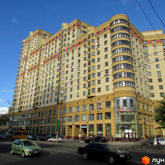 Високоповерхова новобудова ЖК Златоустівський зі світлим фасадом та червоними елементами оздоблення. Будинок розташований біля дороги з автомобілями.