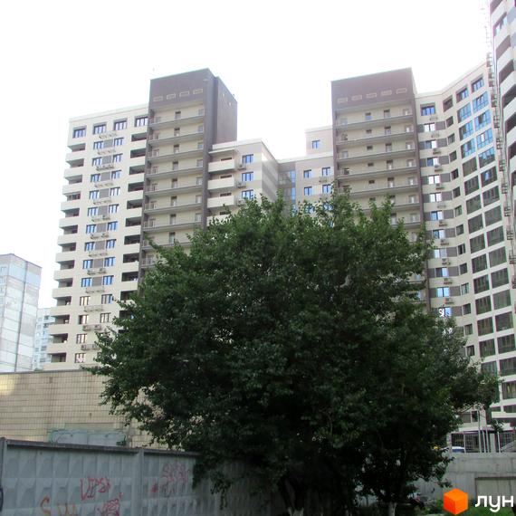 Житловий комплекс Островського, 40 - це багатоповерхові будинки з балконами та кондиціонерами, оточені зеленню. На передньому плані видно бетонний паркан з графіті.