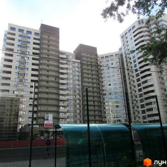 Зовнішній вигляд житлового комплексу Островського, 40, з численними балконами та кондиціонерами. На прибудинковій території видно паркан та зелені накриття.