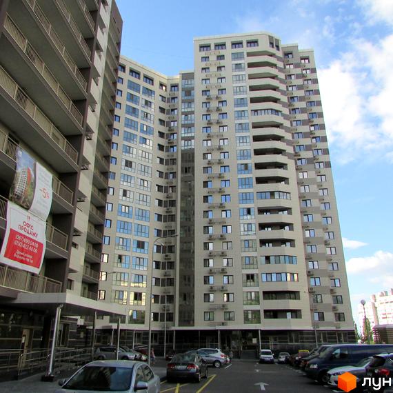 Житловий комплекс Островського, 40 - висотна новобудова з балконами та великою кількістю вікон. Перед будинком розташована парковка з автомобілями.