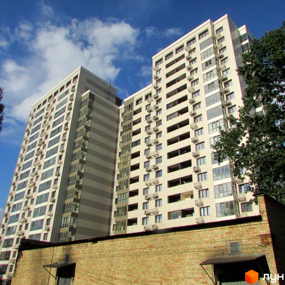 Житловий комплекс Островського, 40 – висотні будинки з численними вікнами та балконами на тлі блакитного неба з хмарами. Перед будівлями розташована цегляна споруда.