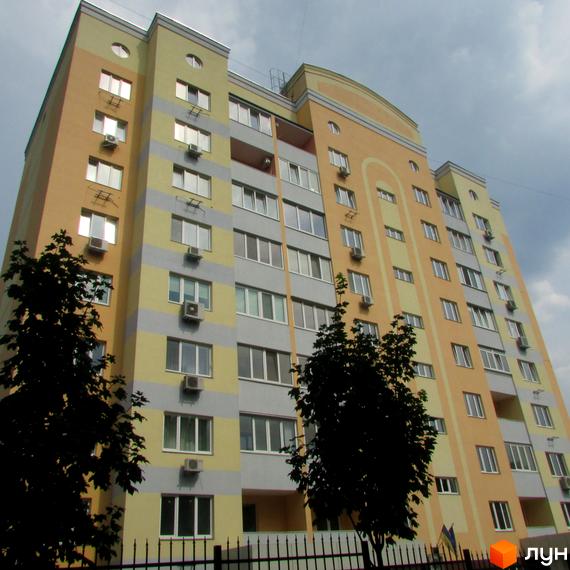 Клубний будинок Gelios - це багатоповерховий житловий комплекс з фасадом у жовтих та сірих смугах. Біля будинку ростуть дерева, а перед ним встановчено паркан.