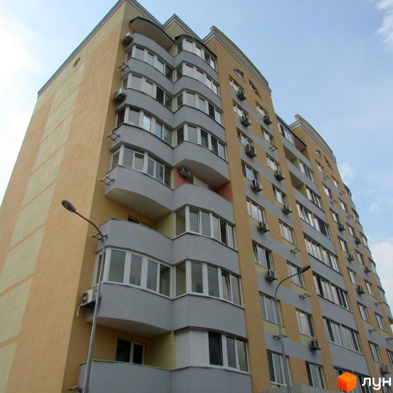 Зовнішній вигляд житлового комплексу Клубний будинок Gelios: багатоповерхова будівля з жовто-сірим фасадом та балконами. Навколо будинку видно елементи прибудинкової території.