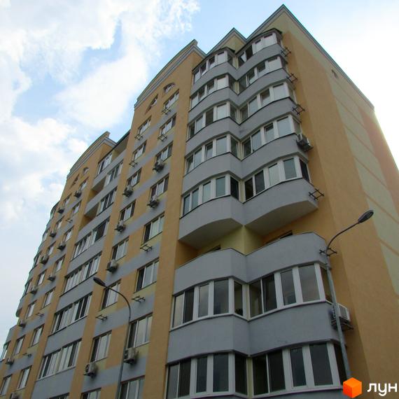 Клубний будинок Gelios - багатоповерхова новобудова з сірими та жовтими фасадами, балконами та кондиціонерами. На тлі блакитного неба з хмарами.