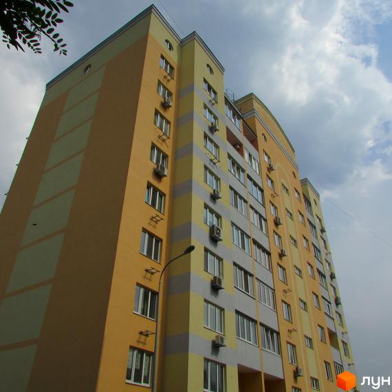 Клубний будинок Gelios – це багатоповерховий житловий комплекс з жовто-сірим фасадом та великою кількістю вікон. Будинок має сучасний вигляд, з кондиціонерами на фасаді.