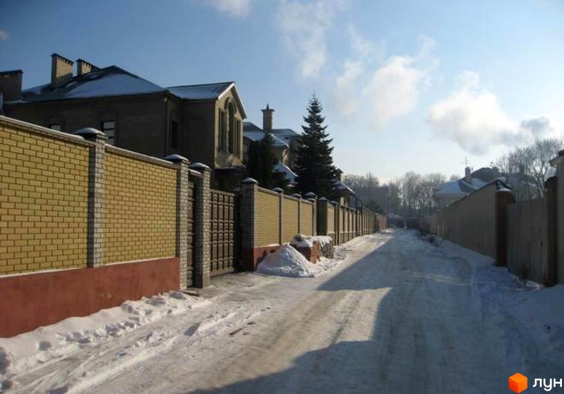 Зимовий пейзаж Котеджного містечка Сокольники. Цегляний паркан з кованими воротами та будинки з снігом на дахах створюють атмосферу затишку.