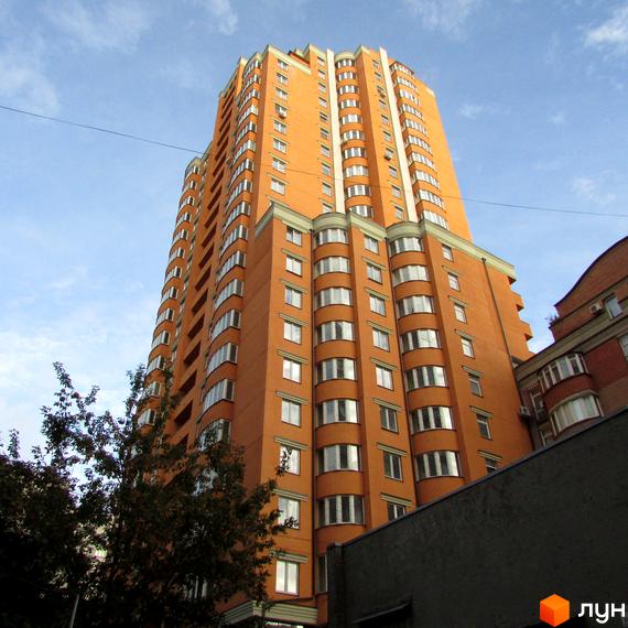 Висотна новобудова ЖК Златоуст з помаранчевим фасадом та численними вікнами. Будинок має вигнуті еркери та білі декоративні елементи. Навколо видно дерева та сусідні будівлі.