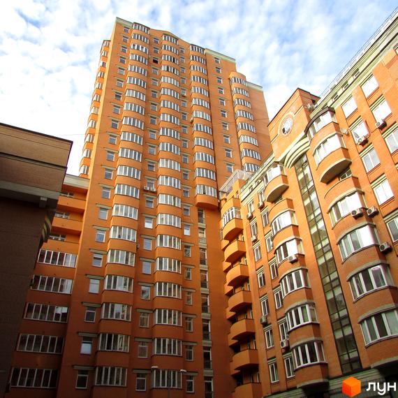 Фасад житлового комплексу Златоуст, висока помаранчева будівля з численними вікнами та балконами, поруч цегляна новобудова.