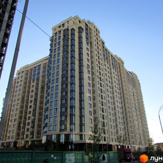 Житловий комплекс Венеція - висотна новобудова світло-бежевого кольору з темними віконними рамами та балконами. Навколо будівлі видно зелені насадження та елементи міської інфраструктури.