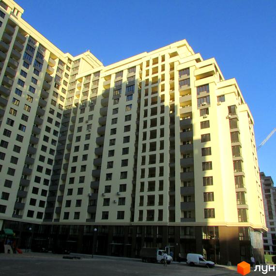 Житловий комплекс Венеція - багатоповерховий будинок світло-жовтого кольору з численними балконами та темними вікнами. На прибудинковій території видно дитячий майданчик та автомобілі.