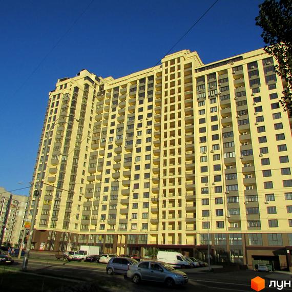 Житловий комплекс Венеція - висотна жовта новобудова з балконами та багатьма вікнами на фоні синього неба. Біля будинку дорога з автомобілями.