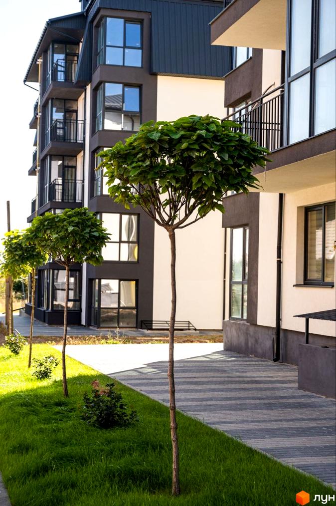 Зовнішній вигляд житлового комплексу Італійський з елегантними фасадами та балконами. Прибудинкова територія з доглянутими деревами та зеленою зоною.