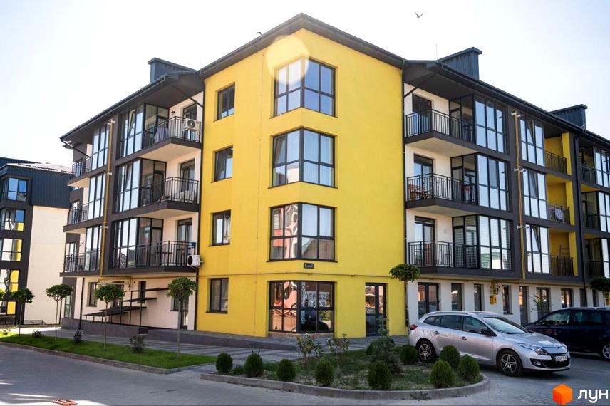 Житловий комплекс Італійський. Фасад будинку жовтого кольору з великими вікнами та балконами. Поруч прибудинкова територія з деревами та автомобілями.