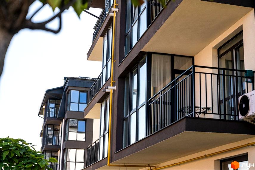 Фасад житлового комплексу Італійський з балконами та великими вікнами. Зовнішній вигляд будинку з жовтими комунікаціями та кондиціонером.