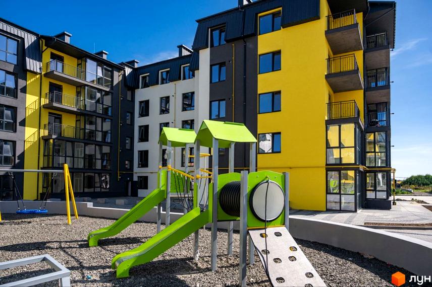 Житловий комплекс Італійський: яскрава жовто-сіра новобудова з балконами та дитячим майданчиком з гірками та гойдалкою.