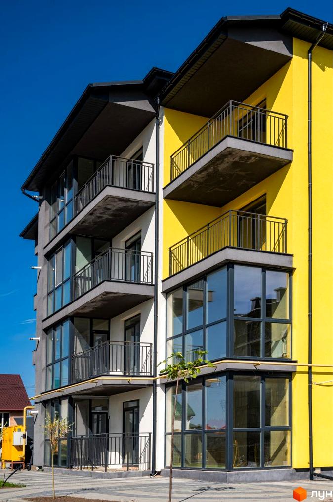 Фасад житлового комплексу Італійський з жовтими та сірими елементами, балконами та великими вікнами. Поряд видно частину прибудинкової території.