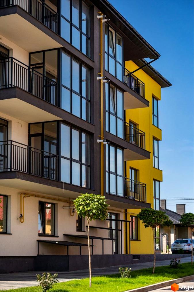 Зовнішній вигляд новобудови ЖК Італійський з жовтими та сірими фасадами, великими вікнами та балконами. Прибудинкова територія з деревами та газоном.