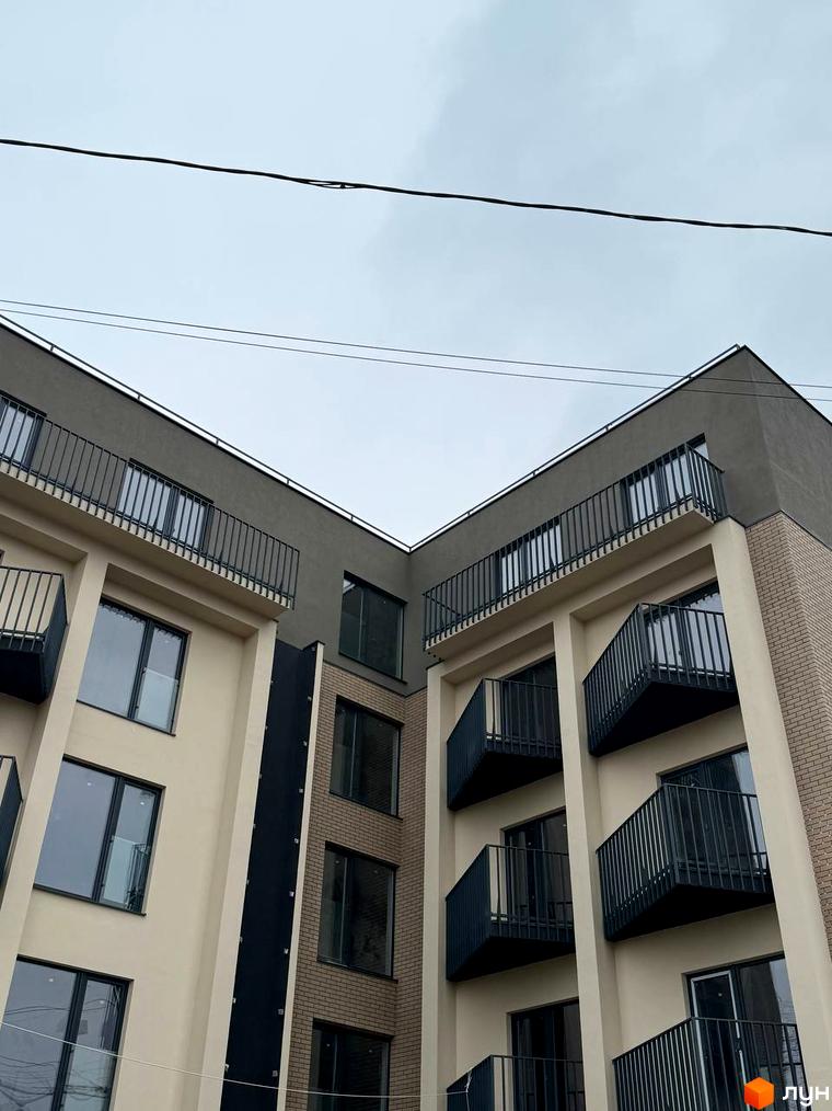 Зовнішній вигляд новобудови ЖК Родовід з балконами та вікнами. Будинок має світло-бежевий та сірий фасади, оздоблені цеглою.