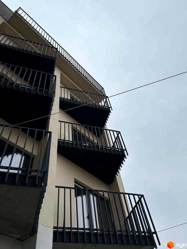 Зовнішній вигляд будинку житлового комплексу Родовід з балконами та огорожею. Фотографія новобудови на фоні сірого неба.