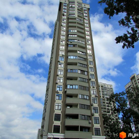 Зовнішній вигляд житлового комплексу Зелений острів-2: висотна будівля з сірими та бежевими фасадами, численними вікнами та балконами. Навколо видно зелені насадження та хмарне небо.