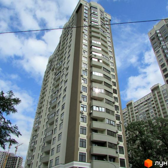 Високий житловий комплекс Зелений острів-2 з численними балконами та великою кількістю вікон. Навколо видно дерева та хмарне небо.