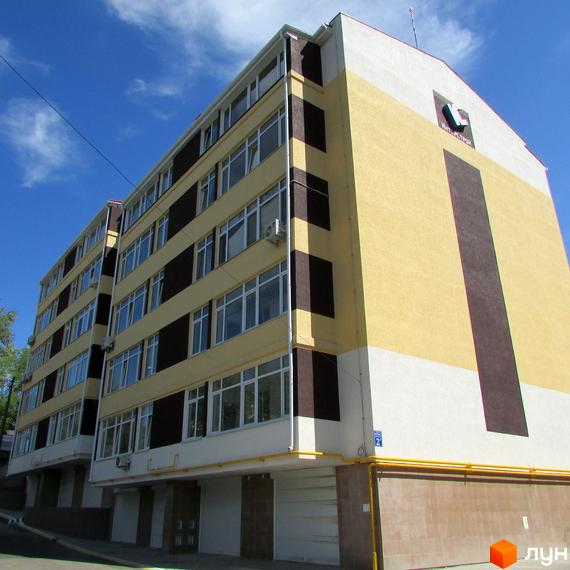 Зовнішній вигляд житлового комплексу Будинок на Бестужева. Багатоповерховий будинок з жовтими, білими та коричневими елементами фасаду. На фасаді великі вікна.