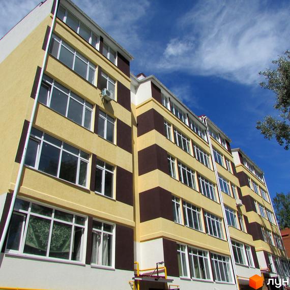 Житловий комплекс Будинок на Бестужева. Фасад новобудови з жовто-коричневими смугами та великою кількістю вікон на тлі блакитного неба.