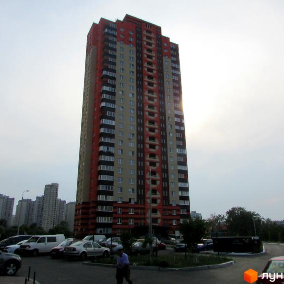 Житловий комплекс на вул. Григоренко, 12а: висотний будинок червоного, бежевого та чорного кольорів з круглими елементами на фасаді, оточений парковкою та зеленню.