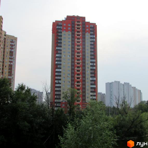 Високий житловий будинок з червоно-бежевим фасадом, темними вставками та круглими елементами. Розташований на вул. Григоренка, 12а, серед дерев.