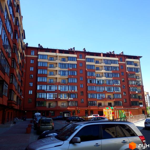 Зображення фасаду багатоповерхового будинку в Житловому комплексі Академмістечко. На передньому плані припарковані автомобілі.