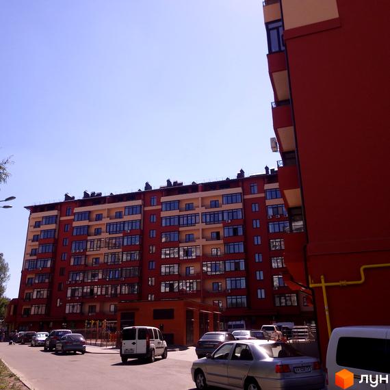 Фото фасаду та подвір'я Житлового комплексу Академмістечко. Багатоповерховий будинок з червоними стінами та великою кількістю вікон, поруч припарковані автомобілі.