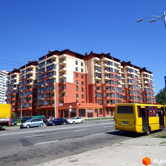 Фото фасаду Житлового району Академмістечко. Багатоповерховий будинок з балконами, поруч дорога з автомобілями та жовтим автобусом.