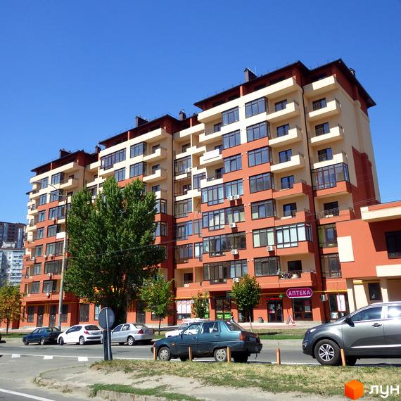 Зображення фасаду Житлового комплексу Академмістечко. Багатоповерховий будинок з балконами та великими вікнами, перед будинком дерева та автомобілі.