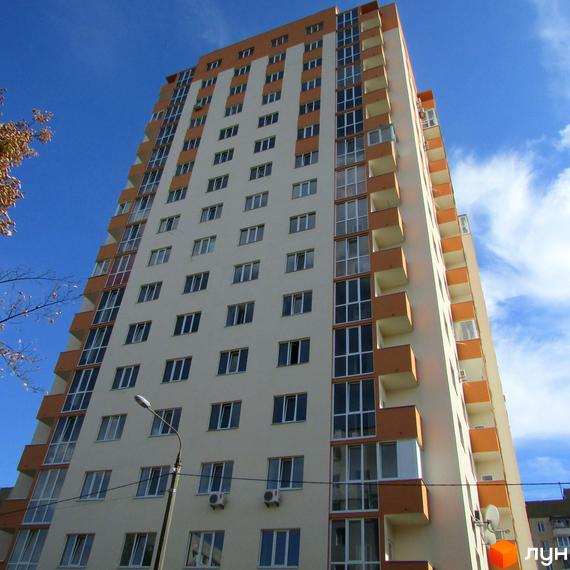 Зображення багатоповерхового будинку Житлового комплексу Мінський на фоні блакитного неба. Вигляд фасаду з вікнами та балконами.