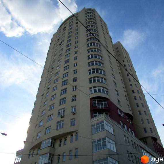 Зображення висотної будівлі Житлового комплексу Будинок на Клименка, що має світло-бежевий фасад з округлими елементами та безліччю вікон.