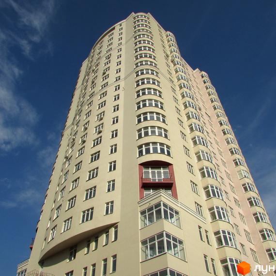 Високий житловий комплекс Будинок на Клименка зі світлим фасадом, численними округлими вікнами та червоним балконом. Будівля на тлі блакитного неба.