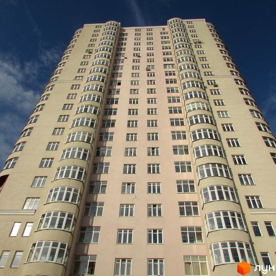 Високий житловий комплекс Будинок на Клименка світлого кольору з численними вікнами та округлими балконами на фоні синього неба.