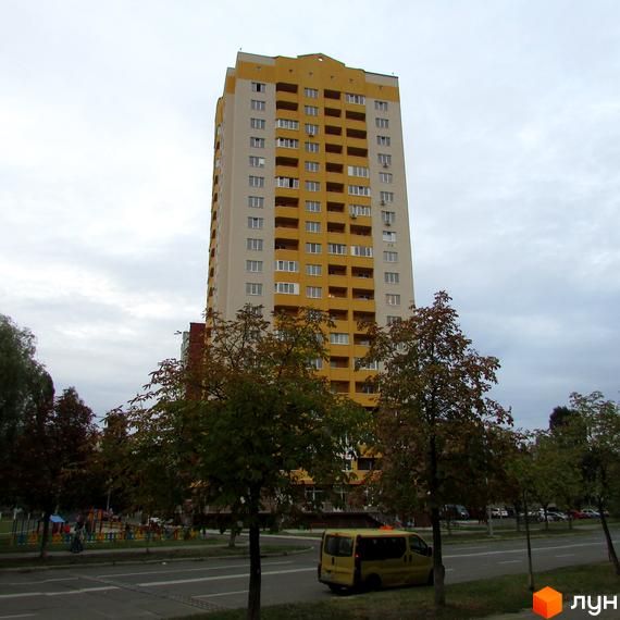 Високоповерховий житловий комплекс на вул. Булгакова, 13 з жовто-білим фасадом та численними балконами. На передньому плані зелені дерева та дорога з автомобілями.