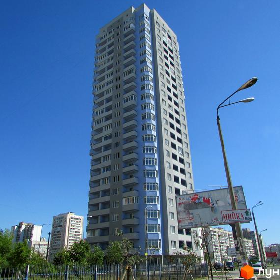 Високоповерховий житловий комплекс на вулиці Гмирі, 17, з сірими та блакитними фасадами та численними балконами. Навколо будинку видно зелені насадження та паркан.