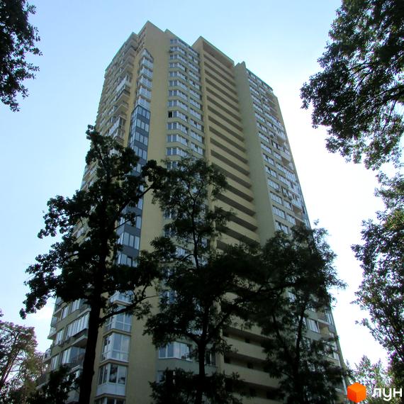 Висотна будівля житлового комплексу на вулиці Верховинній. Фасад будинку світлого кольору з великою кількістю вікон, навколо зелені дерева.