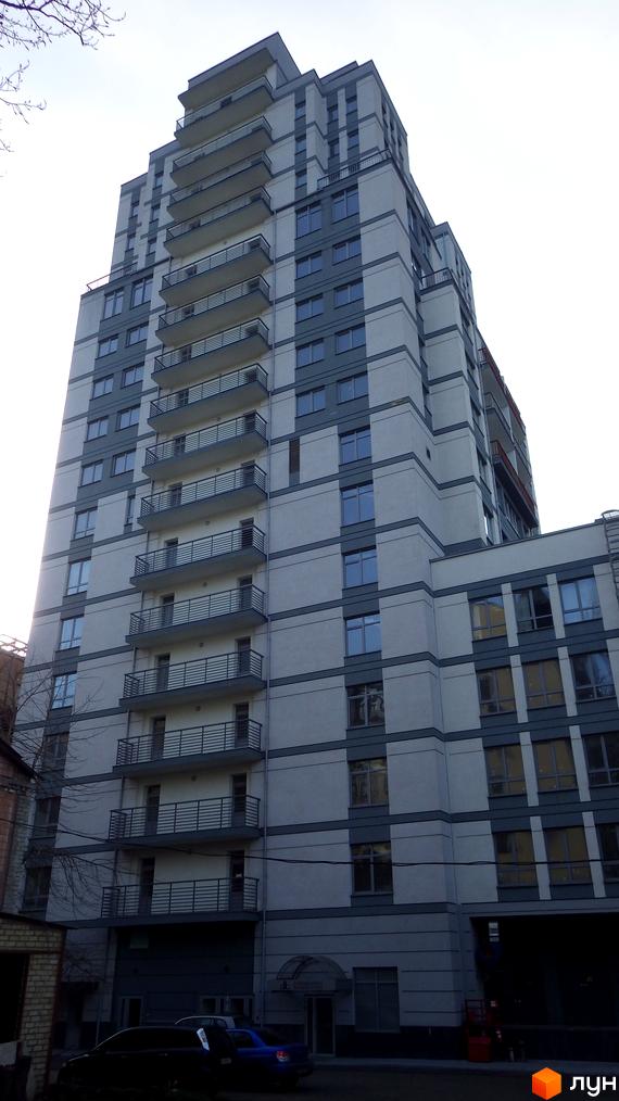 Багатоповерховий житловий комплекс Саксаганський зі світлим фасадом та балконами. Видно прибудинкову територію з припаркованими автомобілями.