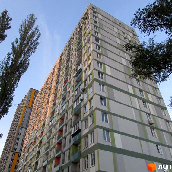 Зовнішній вигляд багатоповерхового житлового комплексу ЖК Грюнвальд з сірими та зеленими смугами. Навколо видно дерева та блакитне небо.