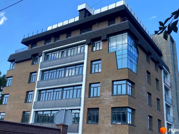 Клубний будинок Donjon – це цегляна новобудова з великими вікнами та балконами, що виходить на блакитне небо.