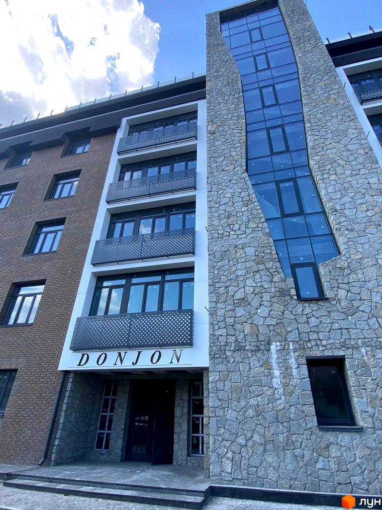 Клубний будинок Donjon з фасадом, оздобленим натуральним каменем та великими вікнами. Перед будинком розташовані сходи та вхідна група.